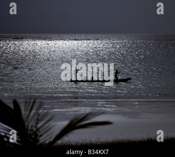 La province de la côte, Kenya, Diani. Trois hommes pole une pirogue au clair de lune dans les eaux peu profondes le long de la plage de Diani. Banque D'Images