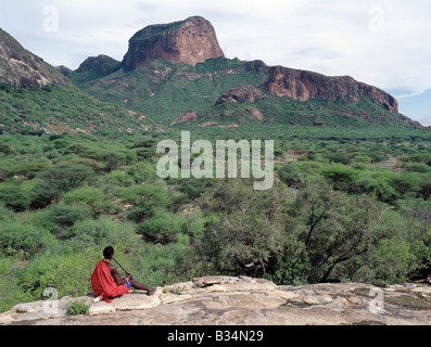 Kenya, Samburu, Ndoto Mountains. Un guerrier Samburu joue un flûte maison donnant sur l'enquête, un rock en fonction Banque D'Images