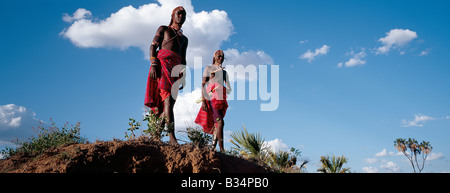 Kenya, Isiolo, Archer's Post. Deux guerriers Samburu resplendissant de longues tresses Ochred et ornements de perles vous détendre dans pose typique à côté d'une rivière. Banque D'Images