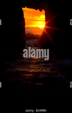 Un océan Pacifique coucher du soleil crée une étoile scintillante à travers un passage voûté à le long de la côte de Big sur Banque D'Images