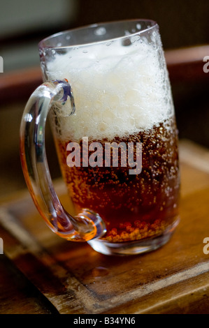 Chope de bière mousseuse, froid, prêt à boire, assis sur un comptoir de bar en bois Banque D'Images