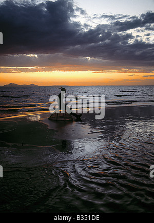 Au Kenya, le lac Turkana, Eliye. Comme le soleil se lève sur le lac Turkana, un pêcheur de Turkana est assise sur son panier de pêche traditionnels d'attendre l'arrivée de ses compagnons de pêche avant que les eaux peu profondes pour le tilapia. Banque D'Images