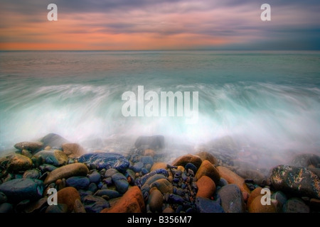 La plage de galets de Riomaggiore à l'aube, les premières lueurs du soleil levant à travers certains profonde lorgnant nuages orageux. Banque D'Images