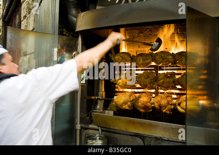 Espagne Barcelone Cook en utilisation uniforme louche pour badigeonner le poulet rôti en cuisson four en brique avec des flammes Banque D'Images