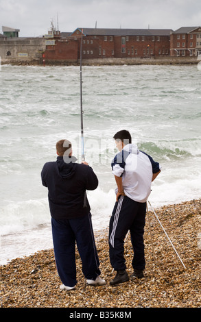 Deux jeunes hommes pêche en mer à partir de la plage de galets à Portsmouth. Banque D'Images