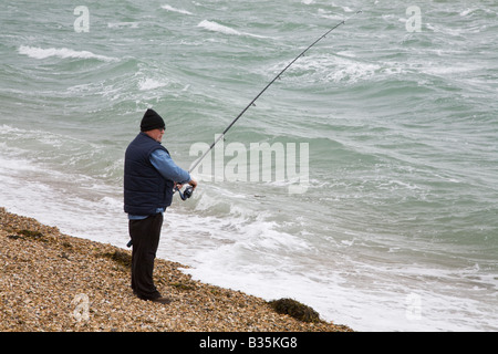 Un pêcheur tenant une canne à pêche au-dessus de vagues sur une plage de galets de Portsmouth. Banque D'Images