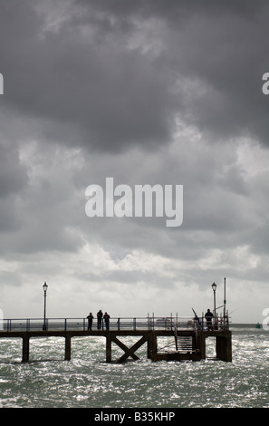 Les gens de la pêche sur une jetée en bois découpé sur un ciel nuageux sur la côte de Portsmouth. Banque D'Images