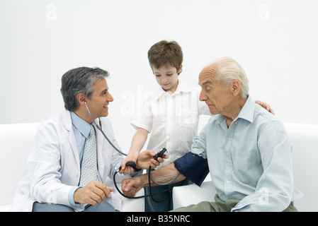 Médecin principal de mesure de la pression artérielle de l'homme, garçon aidant Banque D'Images