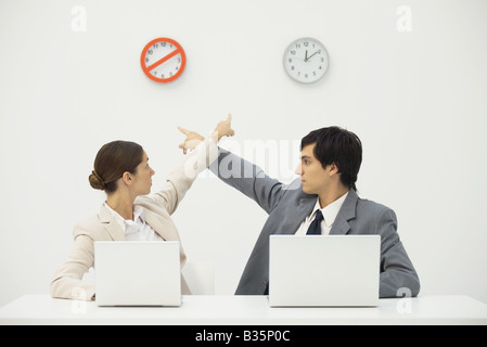 Bagages sitting at desk, pointant sur horloges sur mur derrière eux Banque D'Images