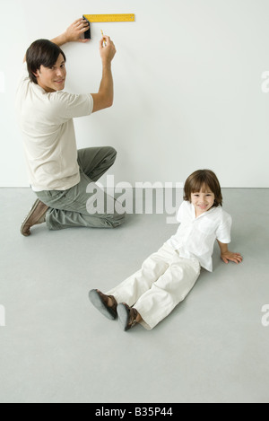 La mesure de l'homme mur avec une règle, le fils assis à proximité, à la fois smiling at camera Banque D'Images