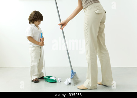 Petit garçon aider sa mère balayer le plancher, cropped view Banque D'Images