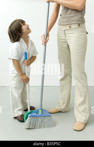 Petit garçon aider sa mère balayer le plancher, cropped view Banque D'Images