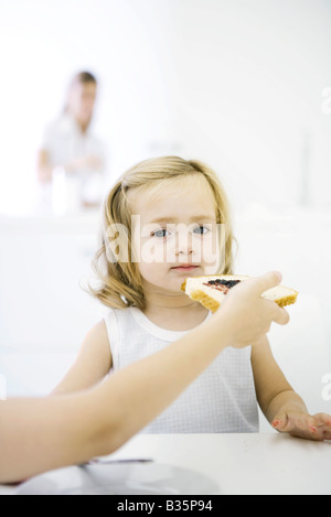 Jeune fille assise à table et être nourri un morceau de pain avec de la confiture, cropped view Banque D'Images