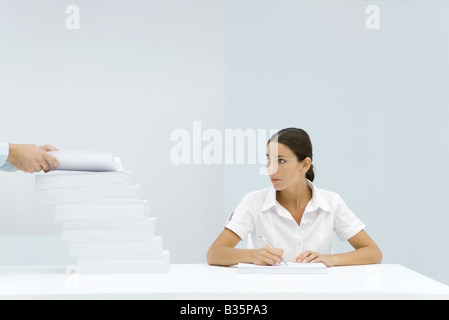 Femme assise à la table, regardant une pile de papier, man's hands ajouter du papier à la pile Banque D'Images