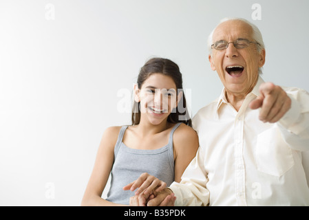 Teenage girl côte à côte avec son grand-père, les deux rient, senior man pointing at camera Banque D'Images