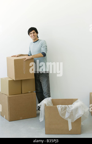 Homme debout par pile de boîtes en carton, smiling at camera Banque D'Images