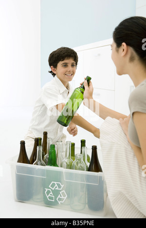 Jeune femme et garçon mise en bouteilles en verre bac de recyclage, smiling at each other Banque D'Images