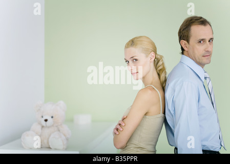 Couple standing back to back en pépinière, à la recherche sur les épaules à l'appareil photo, woman's arms folded Banque D'Images