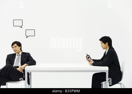 Homme avec des bulles de texte sur la tête assis en face de deuxième homme avec de faux téléphone dans la main Banque D'Images