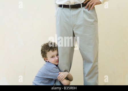 Garçon accroché à la jambe de son père, looking at camera, portrait Banque D'Images