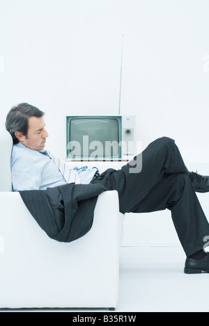 Businessman prendre une sieste dans un fauteuil, vous courber avec les jambes croisées, side view Banque D'Images