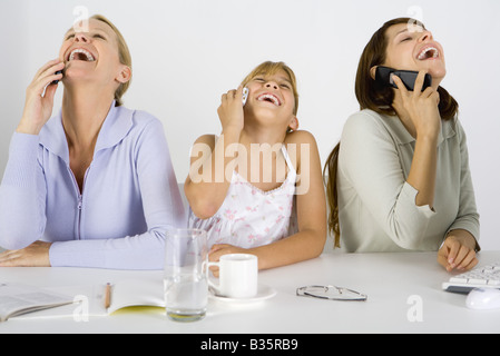 Deux femmes et un preteen girl sitting at table, chacune utilisant un téléphone cellulaire, tous rire et jusqu'à la Banque D'Images