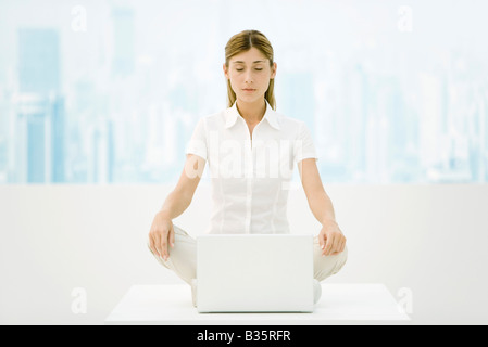 Woman sitting in lotus position sur 24 avec un ordinateur portable, les yeux fermés Banque D'Images