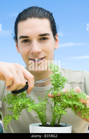 Jeune homme elagage plante en pot, smiling at camera Banque D'Images