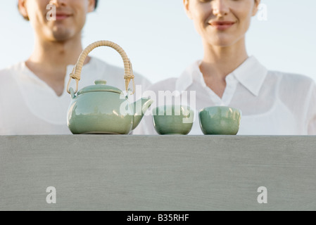 Théière et tasses à thé assis sur le rebord, portrait de l'homme et de la femme en attente à proximité Banque D'Images