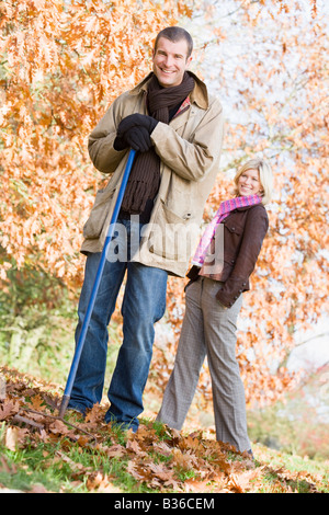 Ramasser des feuilles à l'extérieur de l'homme et la femme en arrière-plan smiling (selective focus) Banque D'Images