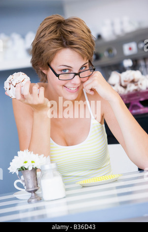 Jeune femme assise à une table en train de manger une petite douceur Banque D'Images