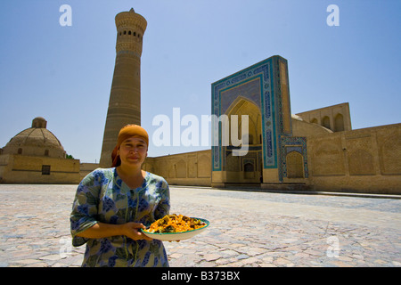 Femme avec Plov en face de la mosquée et Minaret Kalon de Boukhara en Ouzbékistan Banque D'Images