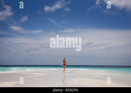 Jeune femme marchant le long de la plage de sable blanc déserte entourée par les eaux tropicales près de l'Inde aux Maldives Banque D'Images