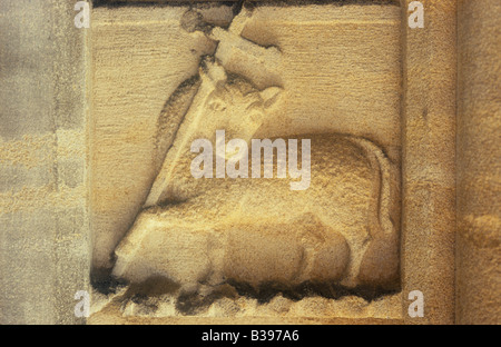 Close up dans une lumière chaude de la sculpture en grès patiné porte de l'église de l'agneau ou du mouton soutenant une épée-comme crucifix Banque D'Images