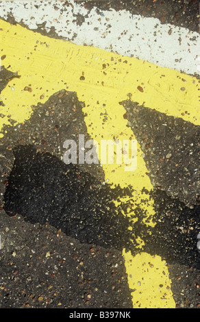 Détail d'une des lignes jaunes et blanches peintes sur la surface goudronnée dans le cadre d'un parking non couvert de peinture antérieure avec grille Banque D'Images