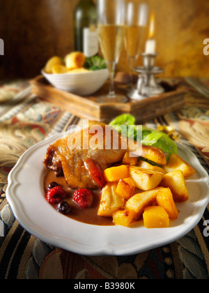 Cuisse de canard au jambon rôti servie avec une sauce aux fruits d'hiver, des pommes de terre rôties et des légumes dans un cadre festif Banque D'Images