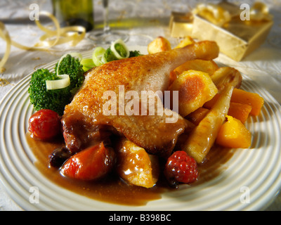 Cuisse de canard au jambon rôti servie avec une sauce aux fruits d'hiver, des pommes de terre rôties et des légumes dans un cadre festif Banque D'Images