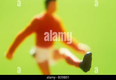 Modèle impressionniste de joueur masculin en chemise rouge et un short blanc avec jambe dans l'air d'avoir des coups de boule avec grass background Banque D'Images