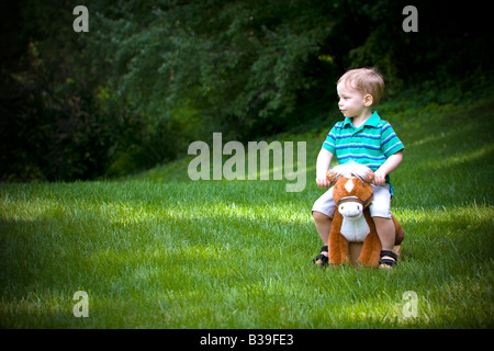 Boy riding un jouet cheval à bascule dans un champ d'arbres en arrière-plan Banque D'Images