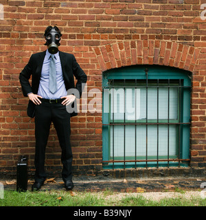 Businessman standing à côté de mur portant masque à gaz Banque D'Images