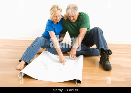 Middle aged couple sitting on floor regarder et discuter ensemble des plans architecturaux Banque D'Images