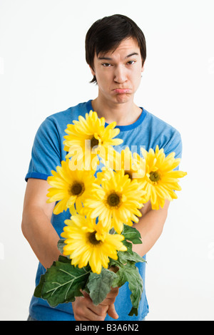 Asian young man holding bouquet de marguerites jaunes avec gerber moue sur son visage Banque D'Images