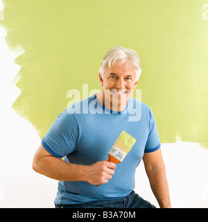 Portrait of smiling man sitting in front of la moitié mur peint avec le pinceau Banque D'Images