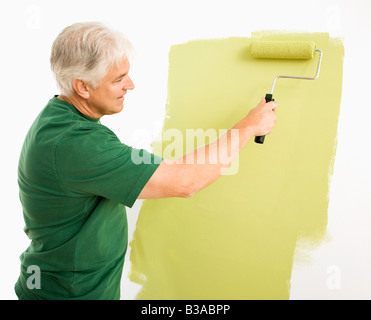 Middle aged man painting wall green with paint roller Banque D'Images