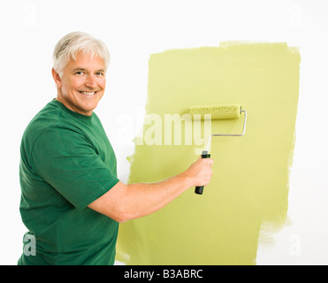 Middle aged man painting wall green with paint roller smiling at viewer Banque D'Images