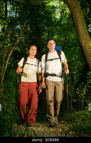 Jeune couple avec sacs à dos randonnée dans un chemin à travers le bois avec les bâtons de trekking forêt près de Bologne Italie Banque D'Images