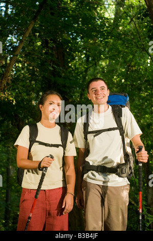 Smiling young couple avec sacs à dos randonnée dans un chemin à travers le bois avec les bâtons de trekking forêt près de Bologne Italie Banque D'Images