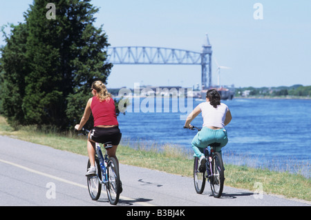 2 Deux personnes femmes équitation à vélo le long du Canal de Cape Cod avec pont à distance Banque D'Images
