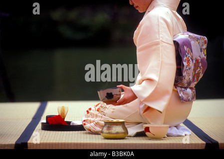 Une femme en kimono assis sur un tatami en céramique plancher tenant un bol à thé la préparation du thé dans une cérémonie de style traditionnel Banque D'Images