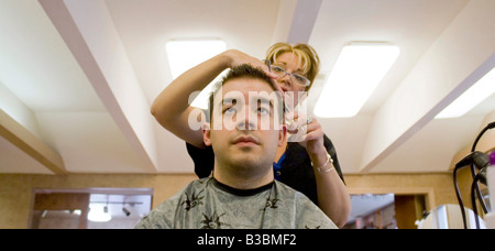 Un jeune homme se fait couper les cheveux par un coiffeur au salon Banque D'Images